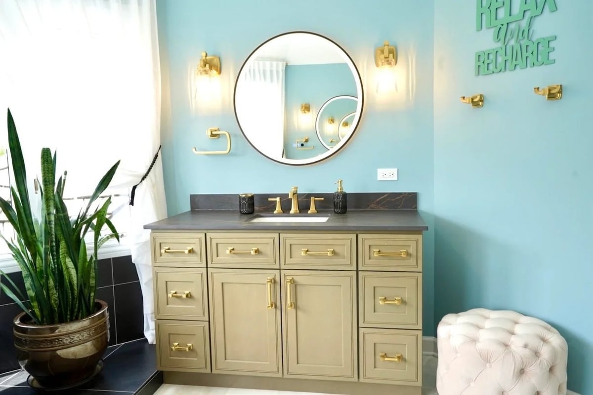 bathroom vanity remodeling in barrington il with sage green cabinetry gold fixtures round mirror wall sconces and dark stone countertop by skor construction