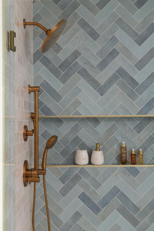 close-up of the Lama primary bathroom shower by Skor Construction in Mount Prospect, IL with blue herringbone tile and brass fix