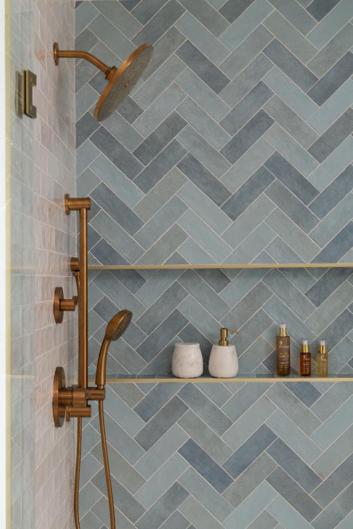 close-up of the Lama primary bathroom shower by Skor Construction in Mount Prospect, IL with blue herringbone tile and brass fix